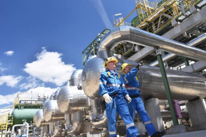 Two oil and gas technicians in PPE inspecting pipework at a processing plant